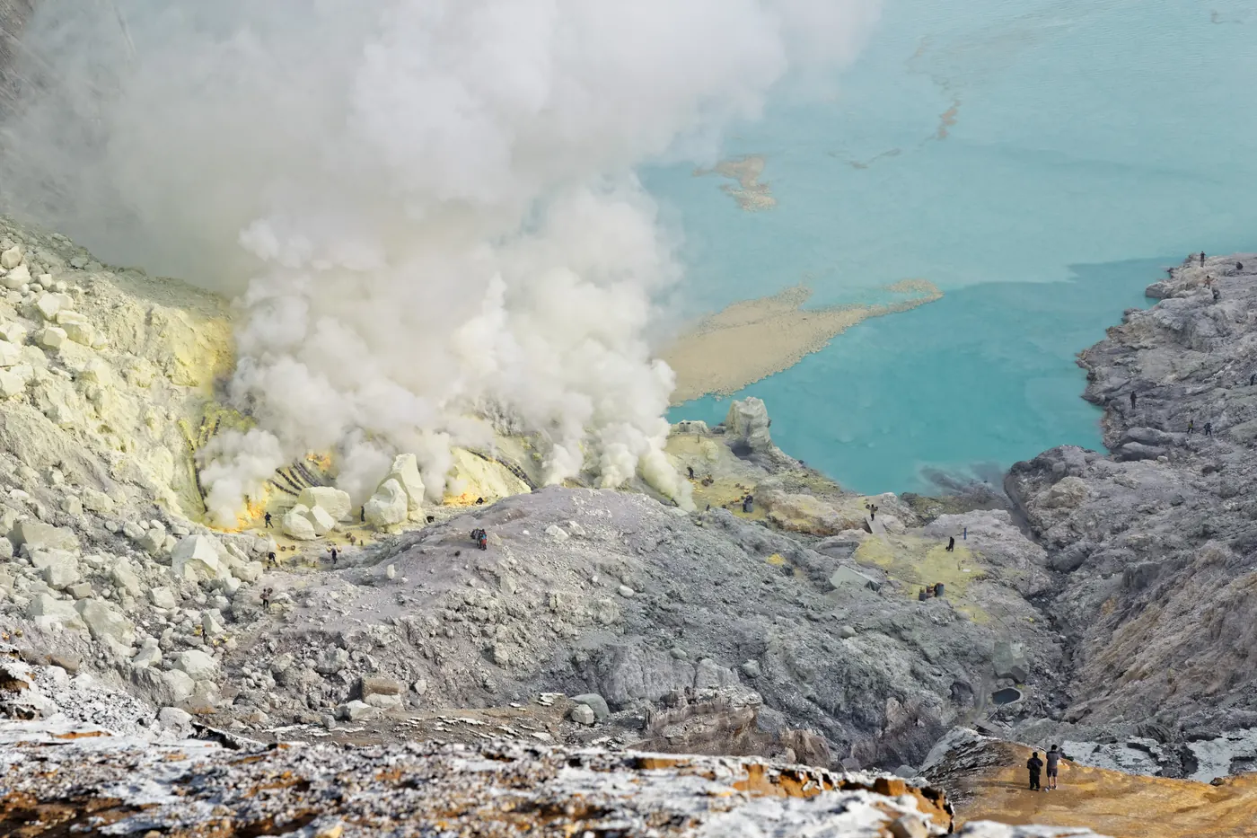 Kawah Ijen dilihat dari atas dengan danau asam berwarna toska, asap belerang, dan penambang di dasar kawah