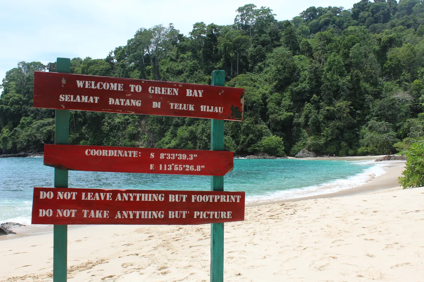 Papan penunjuk Teluk Hijau atau Green Bay di Taman Nasional Meru Betiri dengan pantai berpasir putih dan hutan di belakangnya