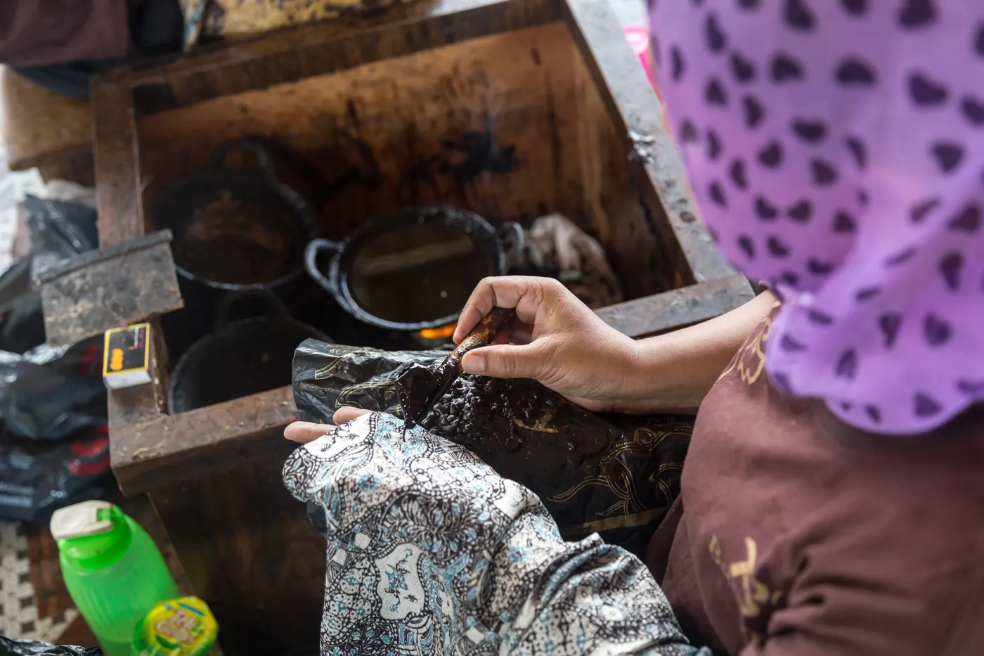 Seorang perajin perempuan mewarnai kain batik yang terbentang di atas meja kerja