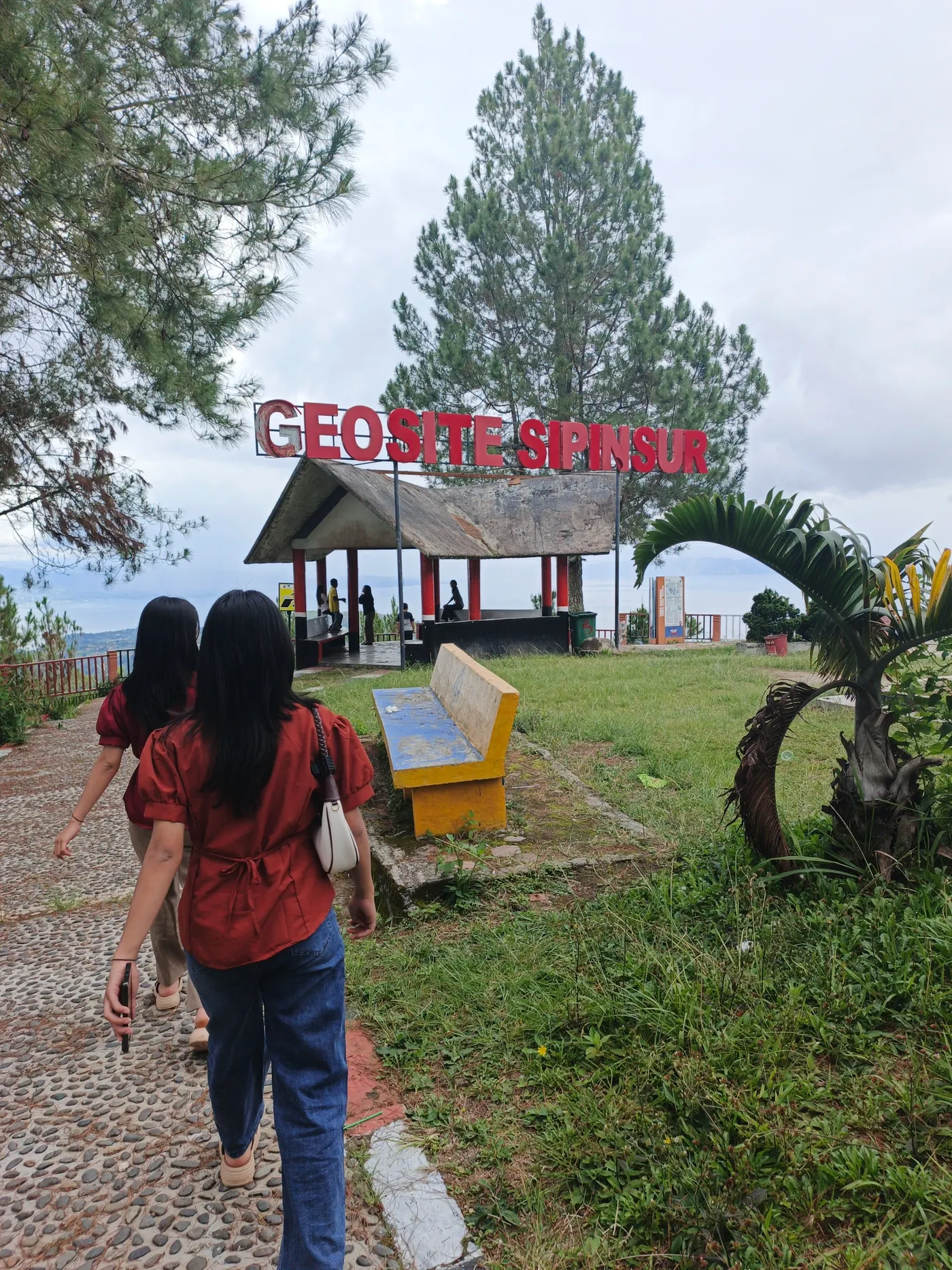 Gerbang bertuliskan Geosite Sipinsur dengan gazebo, bangku, dan tegakan pinus di Paranginan, Humbang Hasundutan