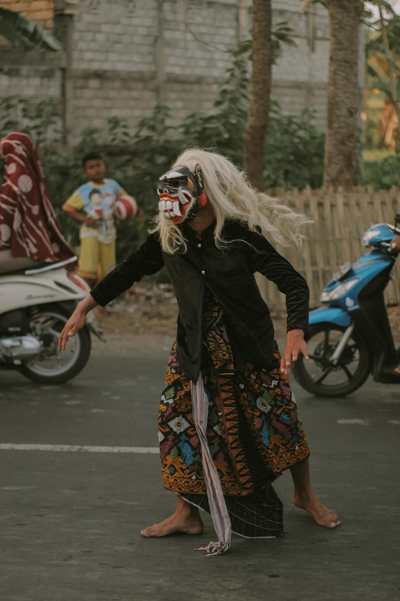 Seorang penari bertopeng dengan kain tenun beriringan di jalan kampung dalam rangkaian Nyongkolan di Lombok