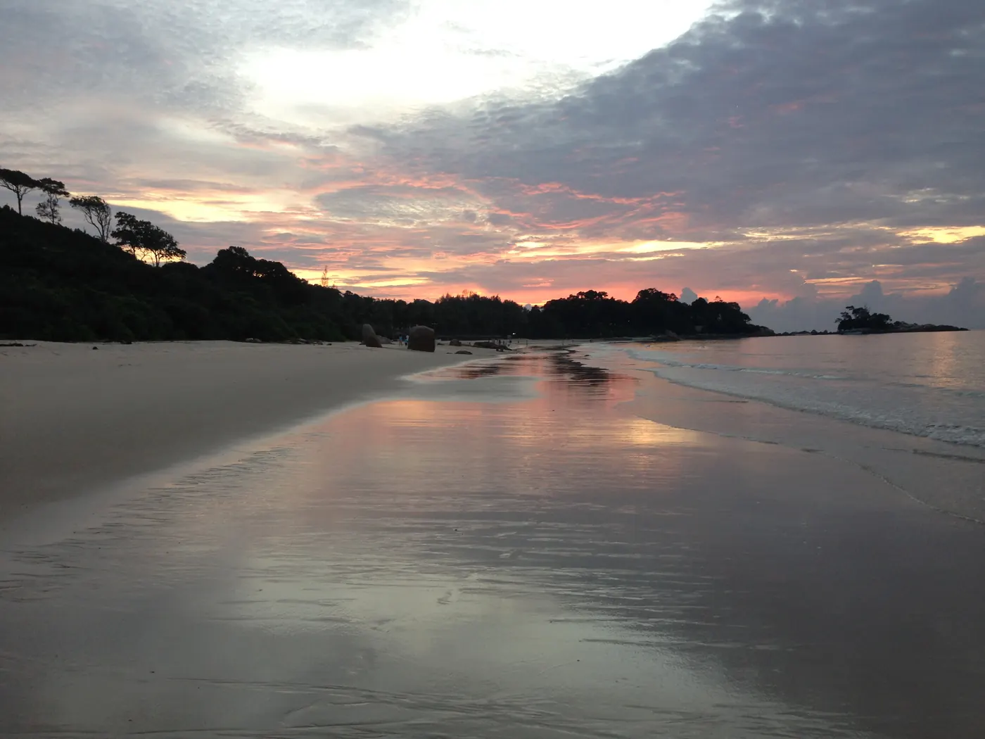 Senja di pantai utara Pulau Bintan, langit jingga terpantul di pasir basah dengan tanjung berhutan di kejauhan
