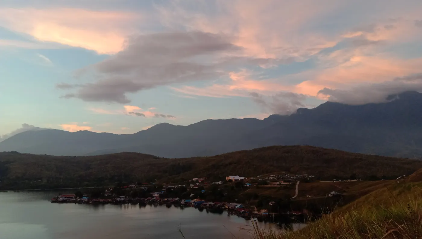 Senja di Danau Sentani dengan kampung di tepi danau dan punggungan Pegunungan Cycloops di kejauhan